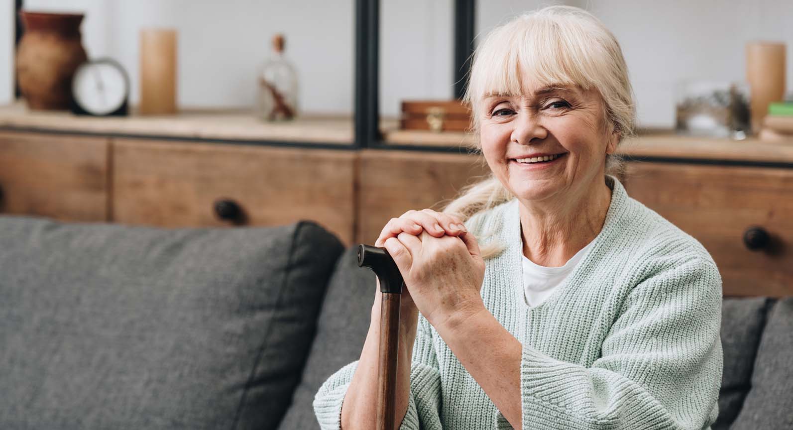 woman smiling, sitting on a couch with a cane in her hand